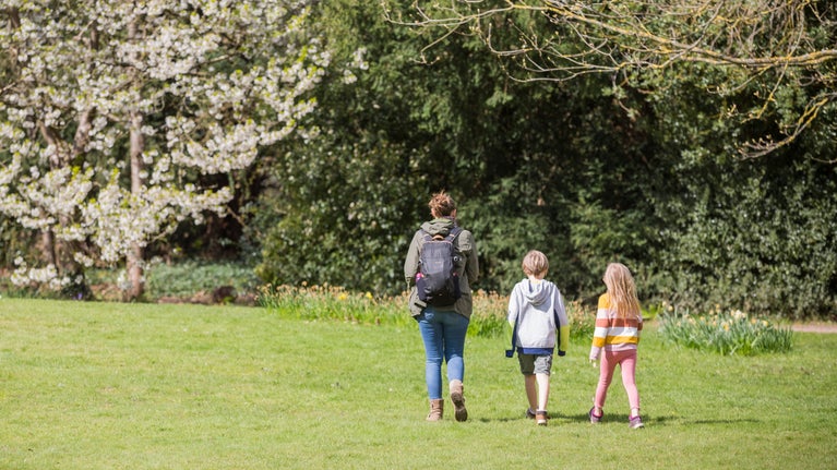 An adult and two children walk about Osterley Park and House, West London with a blossom tree in the background